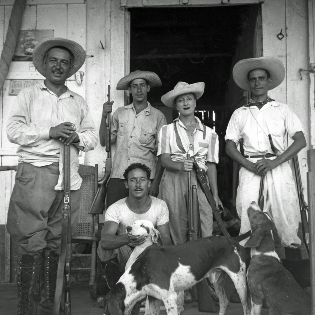 Esperanza and men posing with hunting gear in front of cabin